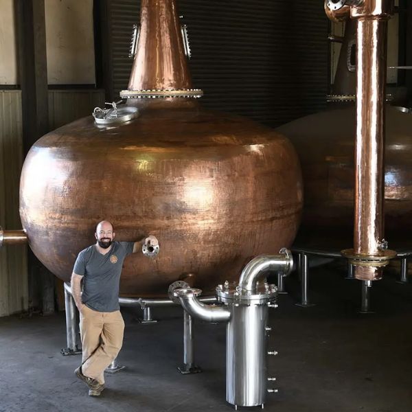 Image: Chip Tate standing in front of his self-crafted copper pot still
